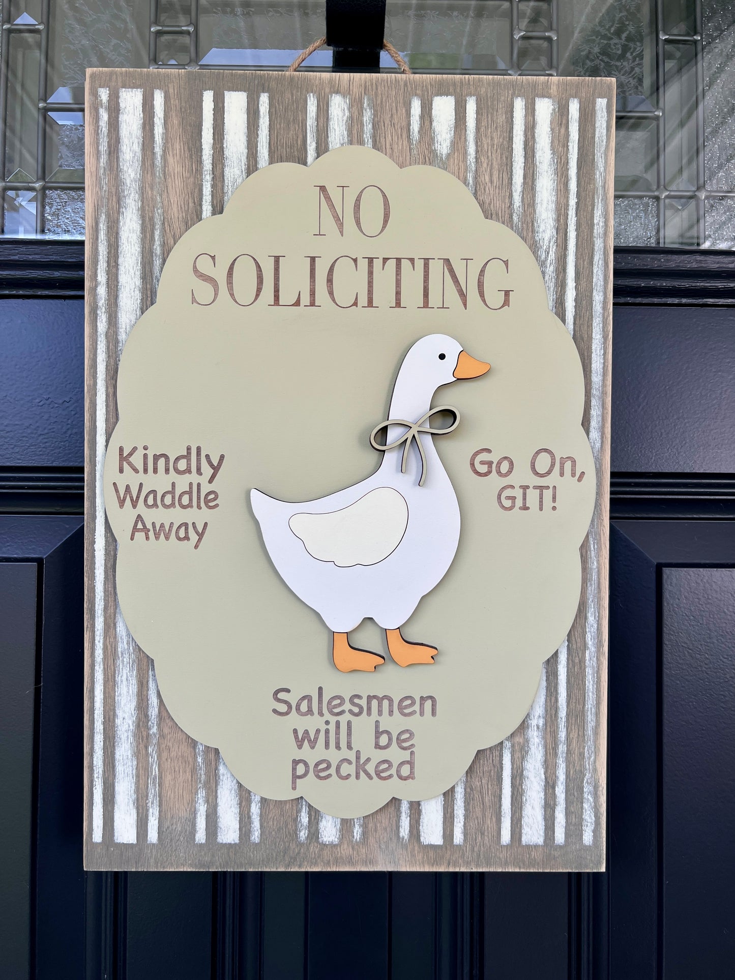 No Soliciting goose door sign full front view on black door showing striped birchwood background and scalloped overlay