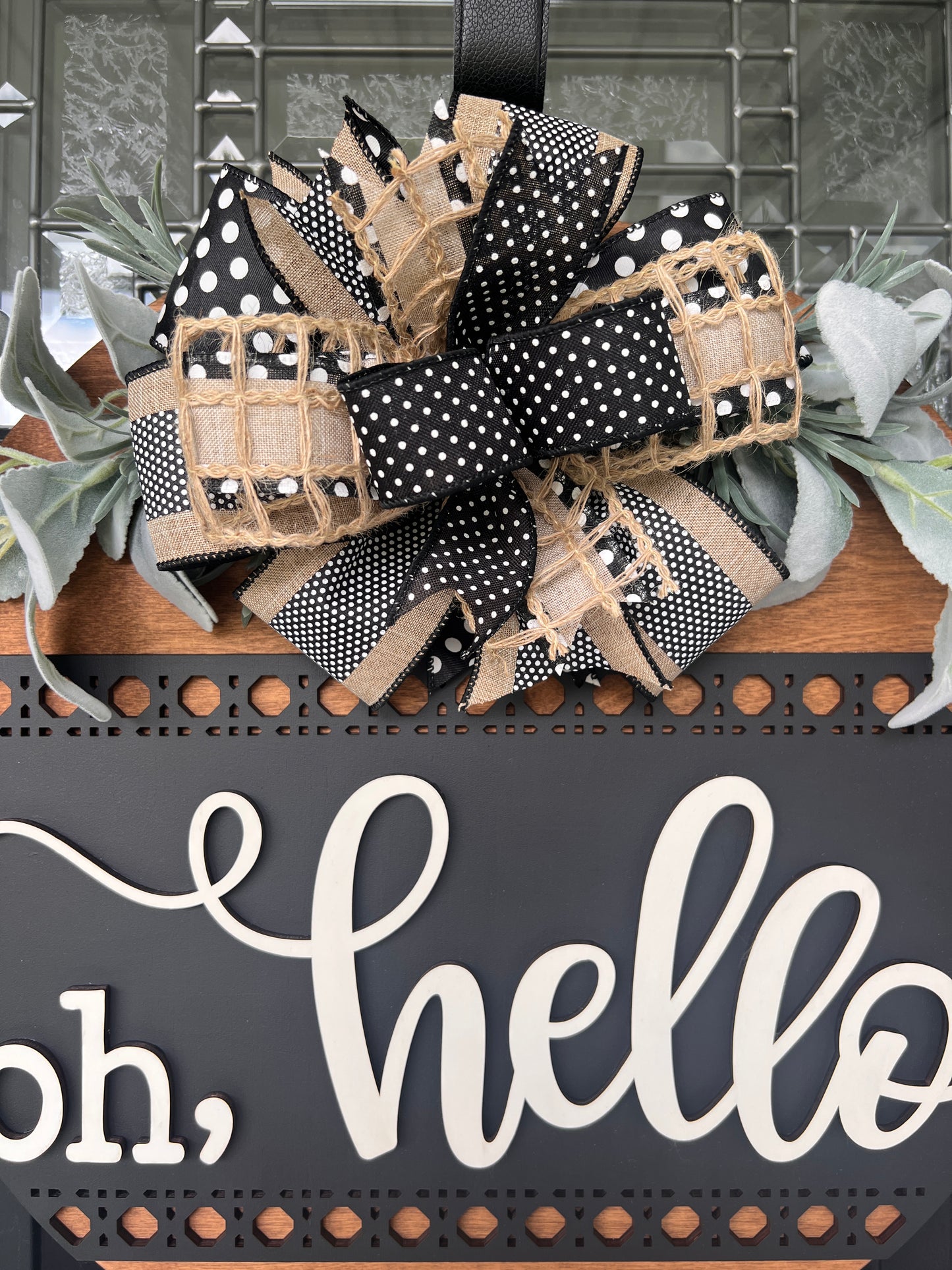 Modern farmhouse Oh Hello wood door hanger displayed on a black front door with designer bow and greenery.