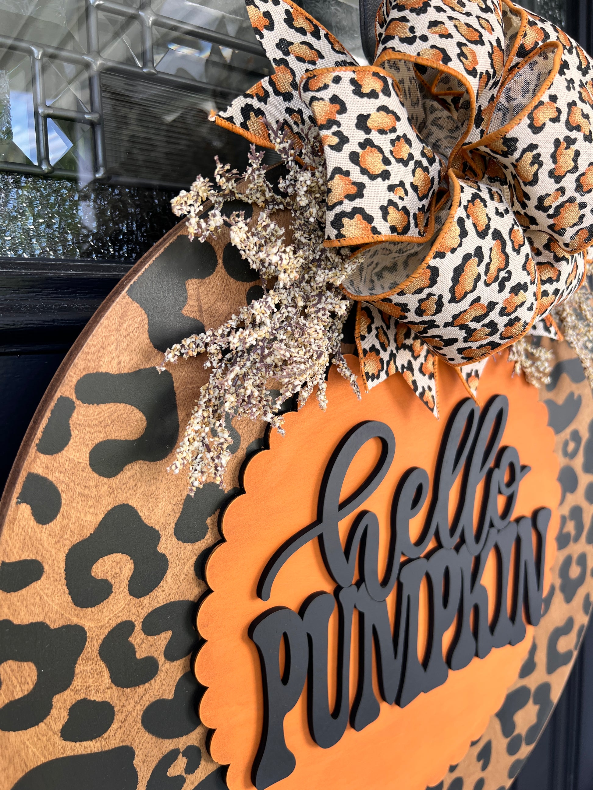 Hello Pumpkin leopard print fall door hanger with layered wood lettering, designer bow, seasonal greenery, and woodgrain animal print background displayed on a front door
