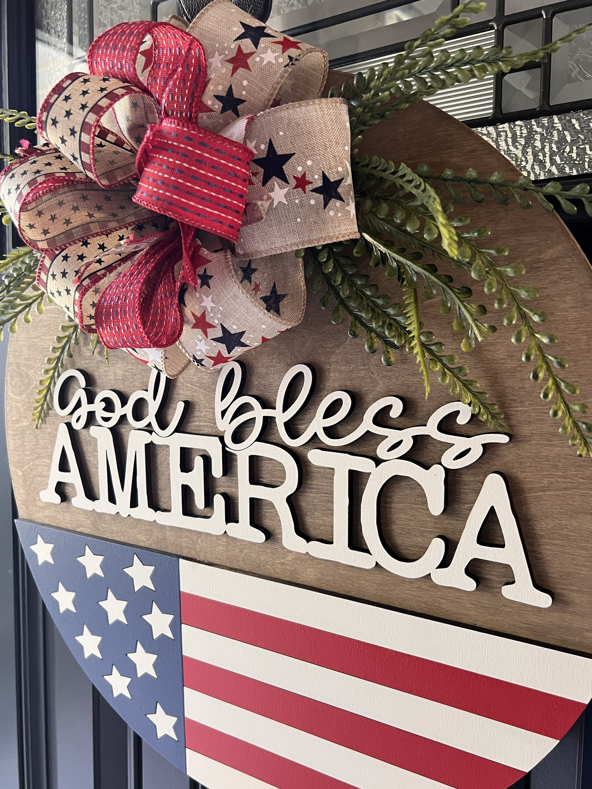 Decorative sign with 'God bless America' text, American flag, and bow on a door.