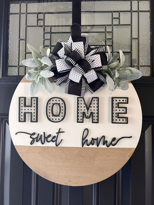 “Home Sweet Home black and white wooden door hanger with layered lettering, decorative bow and greenery on front door”