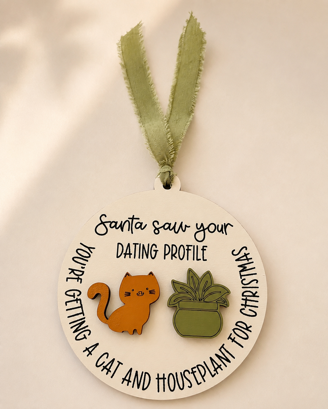 Round Santa Saw Your Dating Profile ornament hanging among evergreen branches and lights