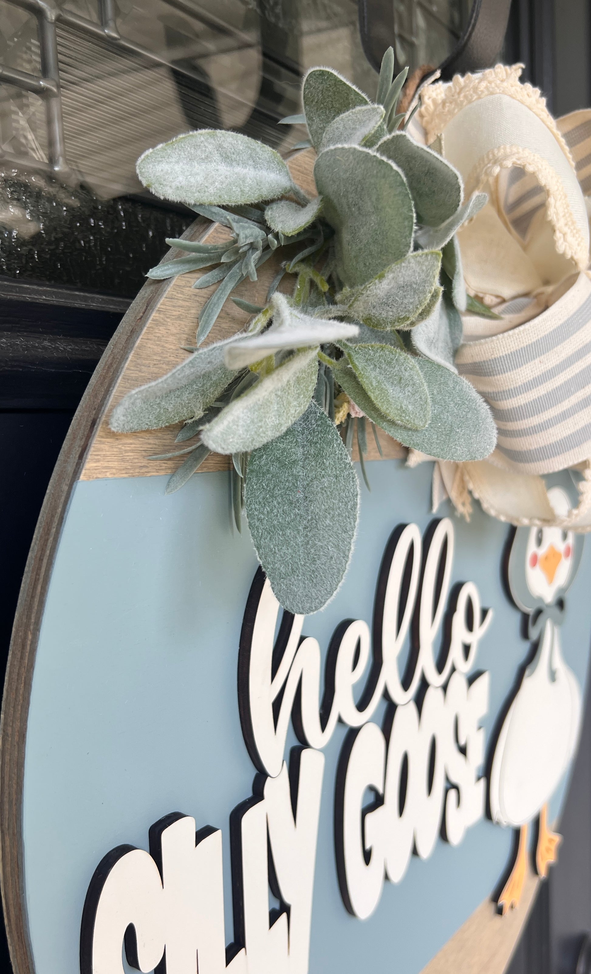 Decorative Goose sign with spring foliage and text 'hello silly goose' on a light blue background with lace accent bow. 