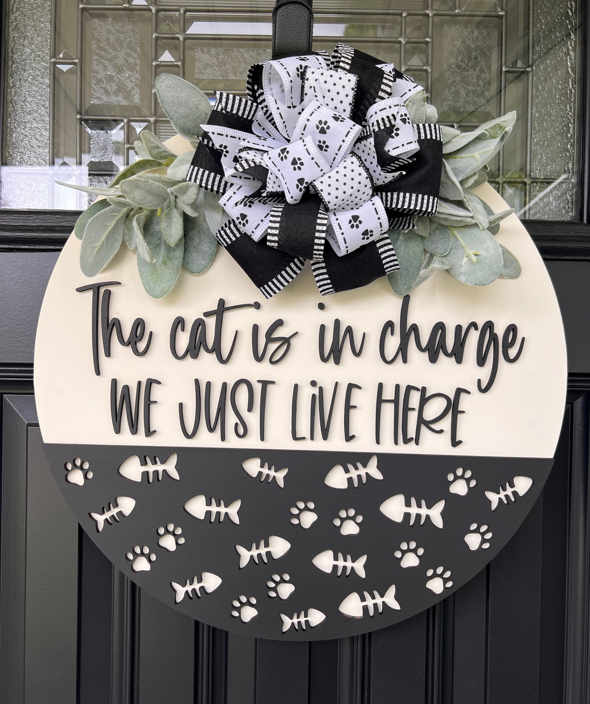 The Cat is in Charge door hanger full view showing cream upper panel with 3D charcoal lettering and charcoal lower panel with paw prints and fish bones