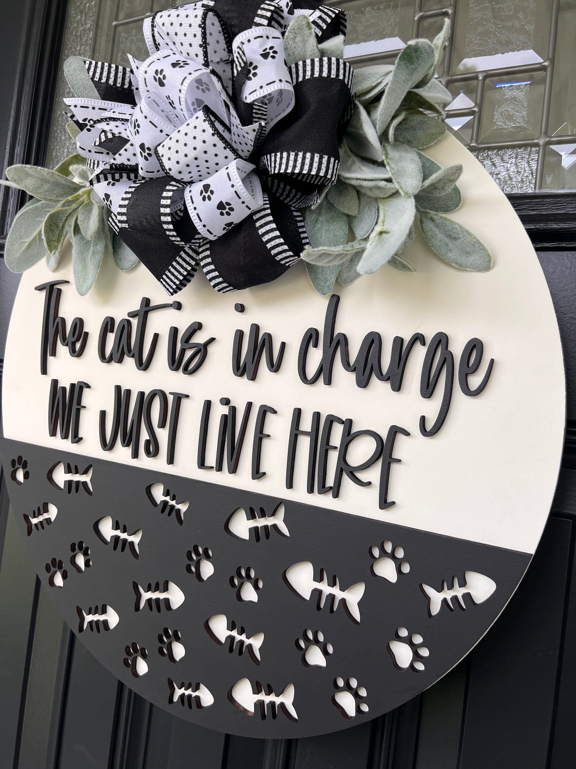 The Cat is in Charge door hanger close up showing layered bow with paw print polka dot stripe and solid black ribbons and lambs ear greenery