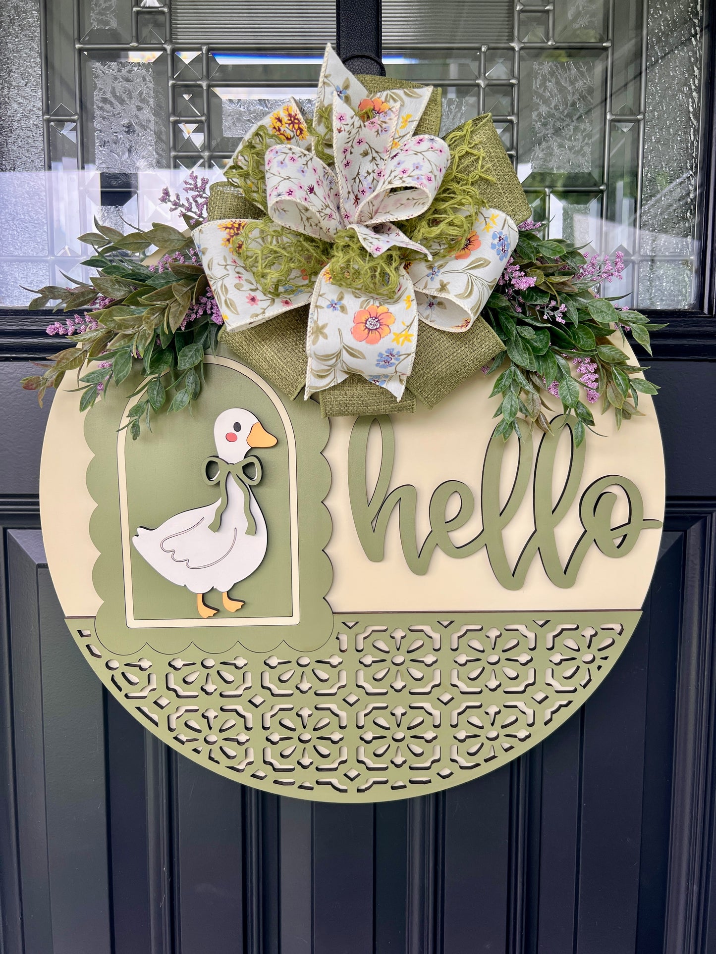 Handmade Hello goose wooden door hanger featuring a vintage white goose, sage green layered lettering, floral bow, laser-cut details, and spring greenery on an 18-inch round front door sign.