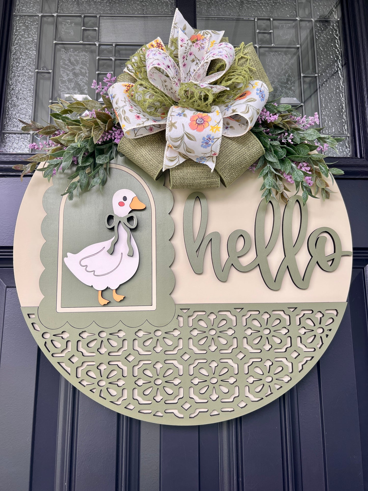 Front view of a handcrafted Hello goose door hanger with dimensional wood lettering, vintage goose design, sage green accents, floral greenery, and an oversized designer spring bow.