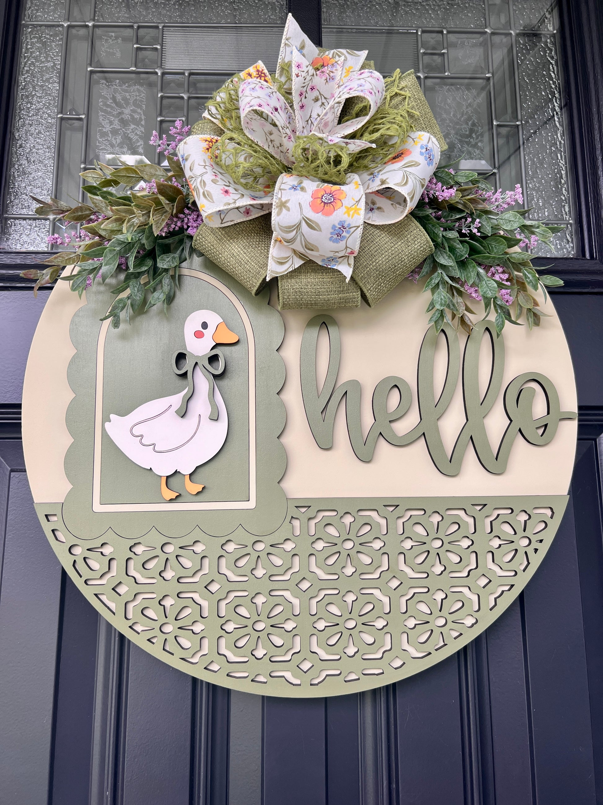 Front view of a handcrafted Hello goose door hanger with dimensional wood lettering, vintage goose design, sage green accents, floral greenery, and an oversized designer spring bow.