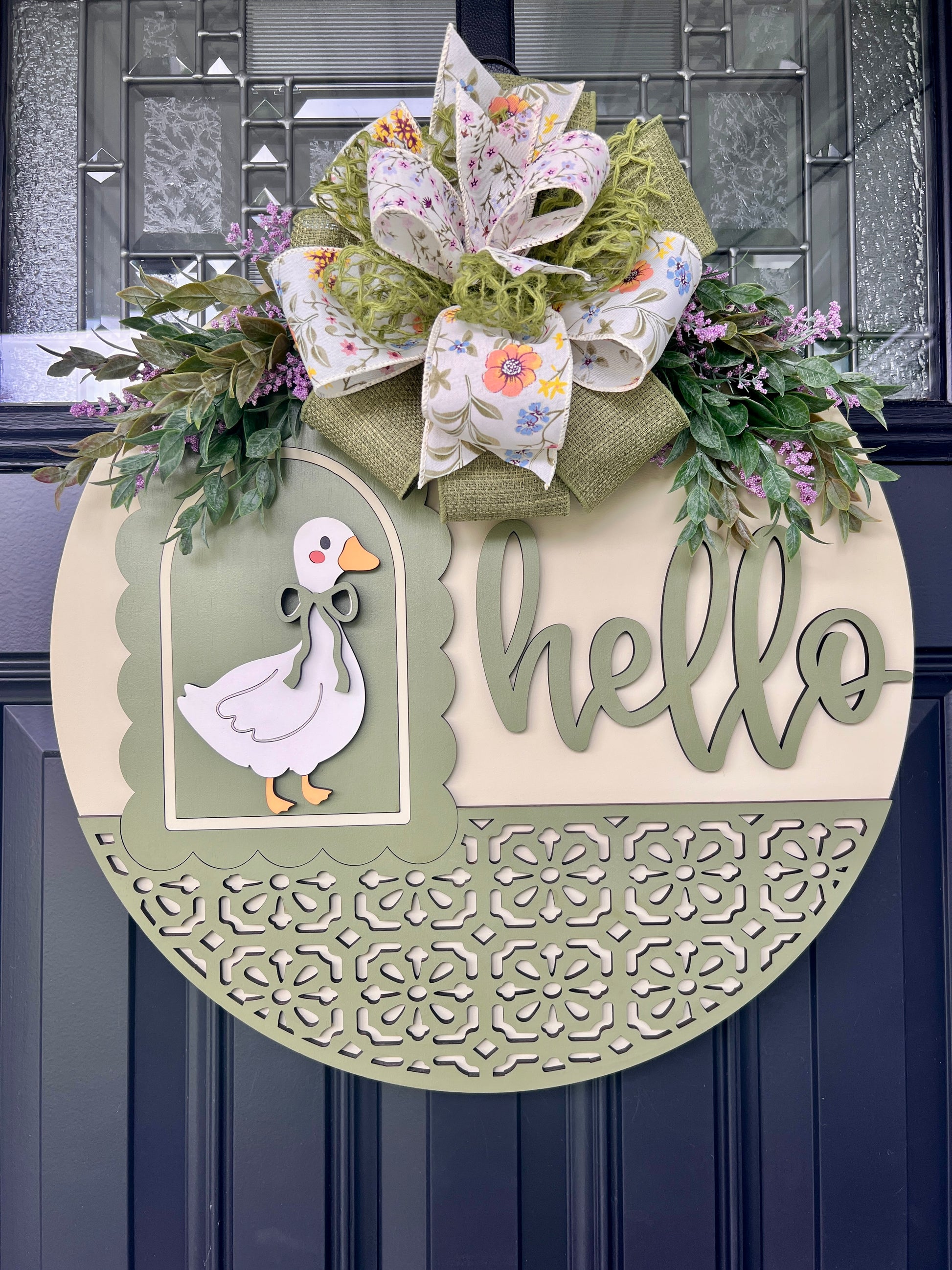 Close-up of handcrafted spring goose front door décor with laser-cut wood details, dimensional Hello lettering, floral ribbon bow, and decorative greenery.