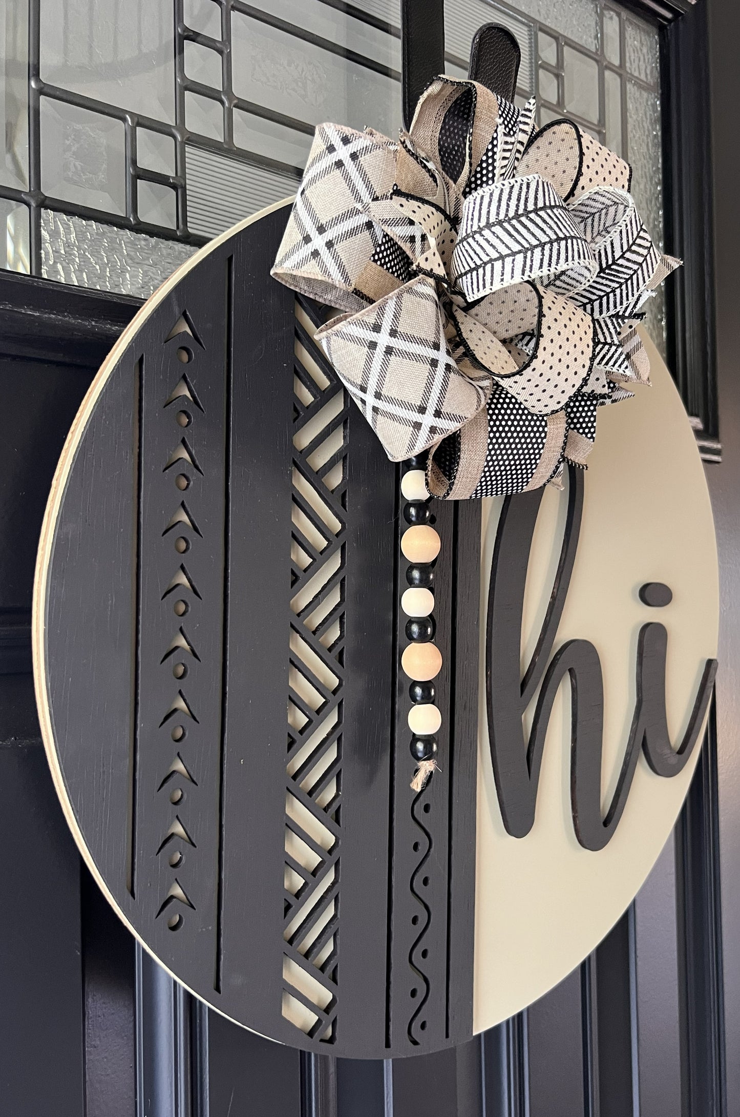 Decorative door hanger with a bow and 'hi' text in raised black lettering on a black front door 
