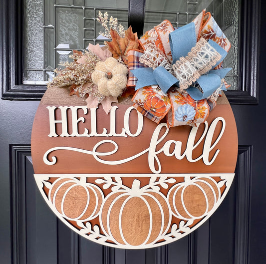 Hello Fall pumpkin door hanger with layered wood lettering, decorative pumpkin cutouts, designer bow, seasonal greenery, and autumn accents. 