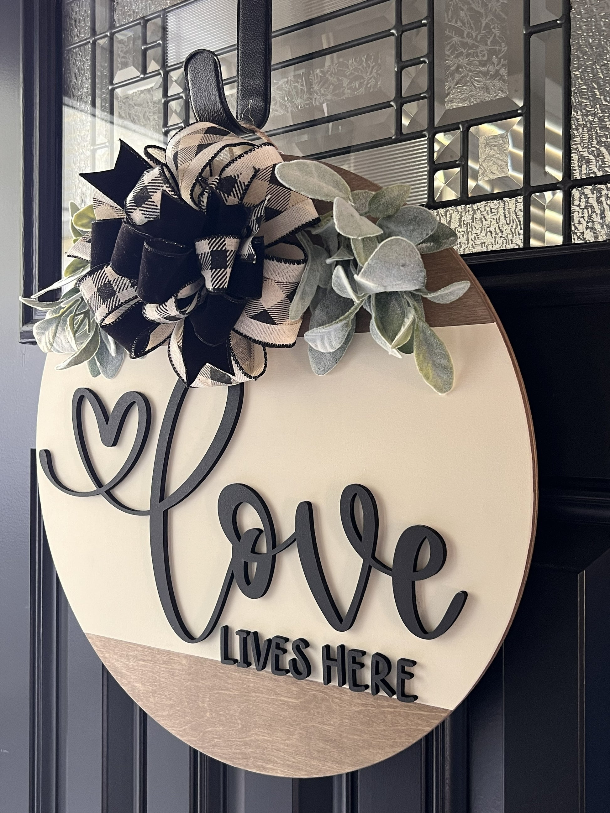 Decorative sign with 'Love Lives Here' in black 3-D lettering with Bow and floral accents on a front door.