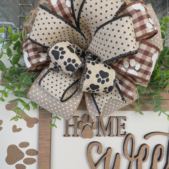 Handmade Home Sweet Home dog lover door hanger featuring laser-cut paw prints, dog bone accents, stained birchwood details, greenery, and a coordinating designer bow. 