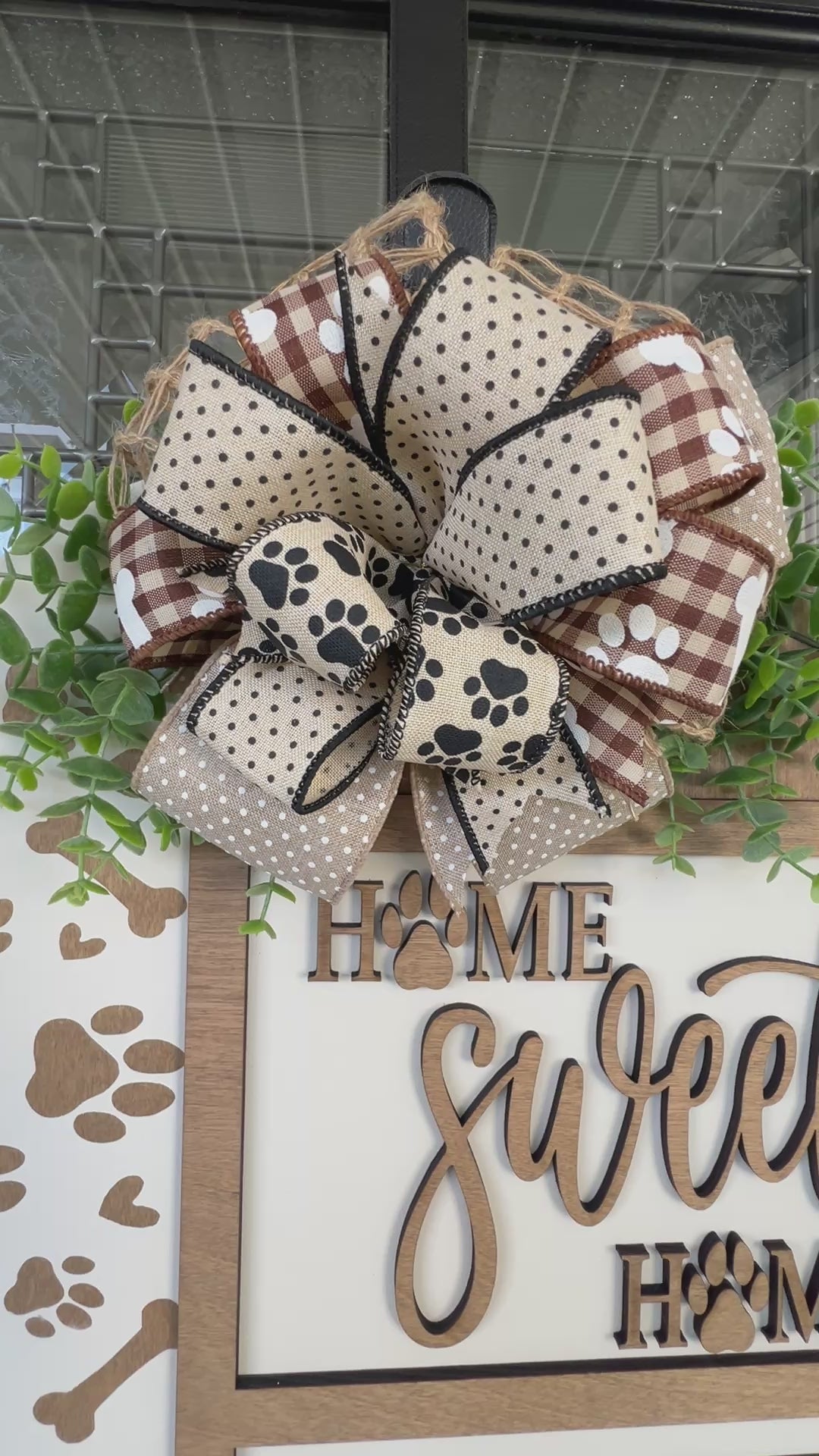 Handmade Home Sweet Home dog lover door hanger featuring laser-cut paw prints, dog bone accents, stained birchwood details, greenery, and a coordinating designer bow. 
