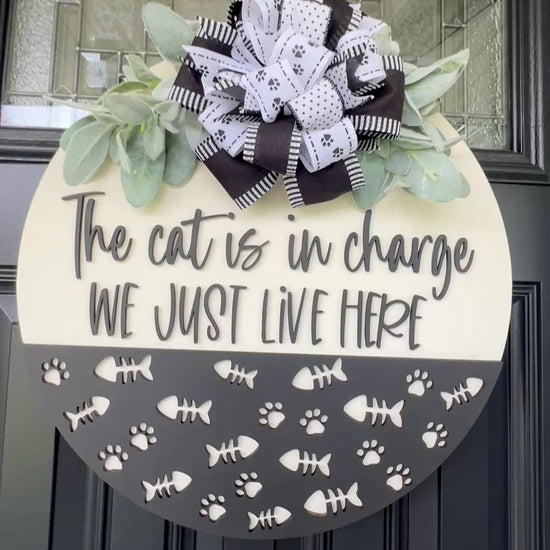The Cat is in Charge We Just Live Here door hanger on black front door with paw print bow and lambs ear greenery