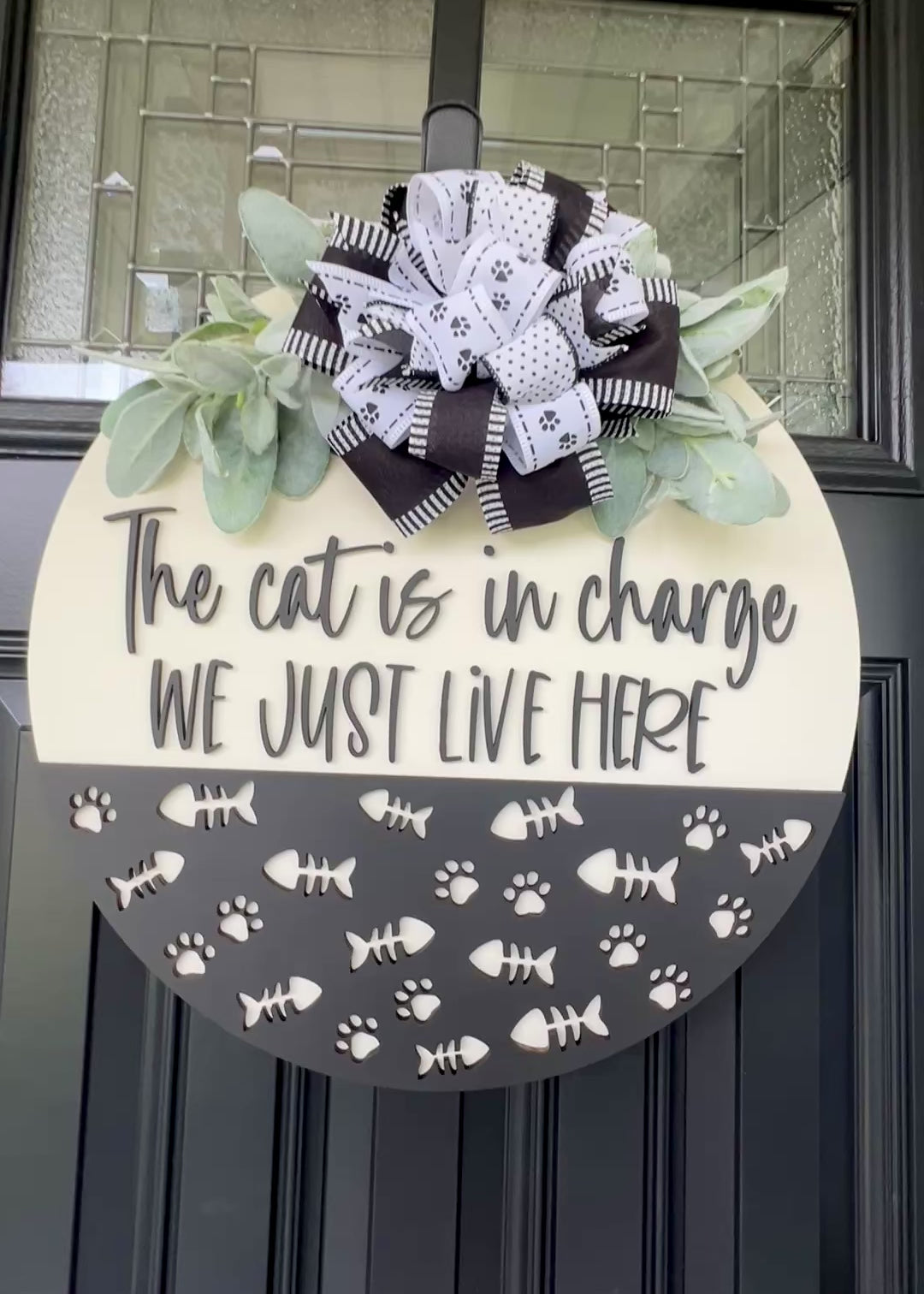 The Cat is in Charge We Just Live Here door hanger on black front door with paw print bow and lambs ear greenery
