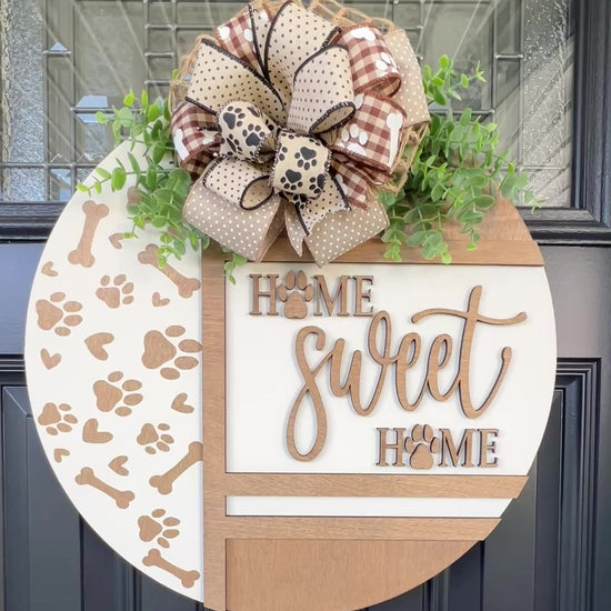 Handmade Home Sweet Home dog lover door hanger featuring laser-cut paw prints, dog bone accents, stained birchwood details, greenery, and a coordinating designer bow. 