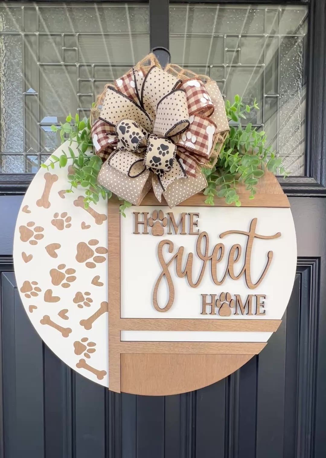 Handmade Home Sweet Home dog lover door hanger featuring laser-cut paw prints, dog bone accents, stained birchwood details, greenery, and a coordinating designer bow. 