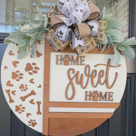 Handmade Home Sweet Home dog lover door hanger featuring laser-cut paw prints, dog bone accents, stained birchwood details, greenery, and a coordinating designer bow.