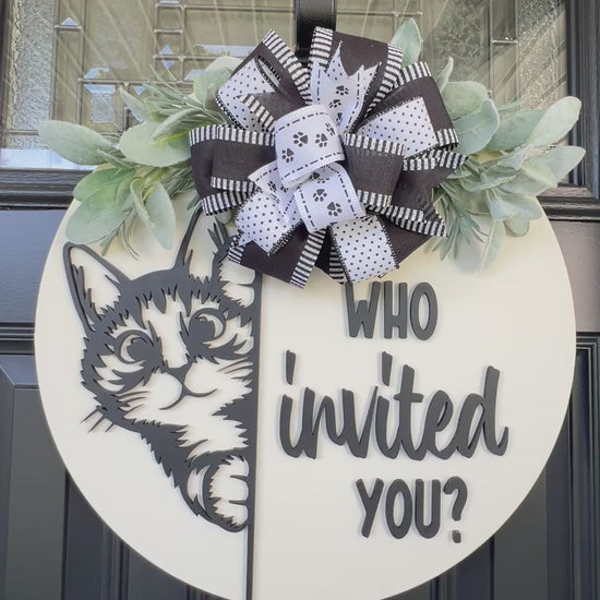 Funny cat door hanger featuring a black cat peeking around the edge and the phrase "Who Invited You?" displayed on a front door.