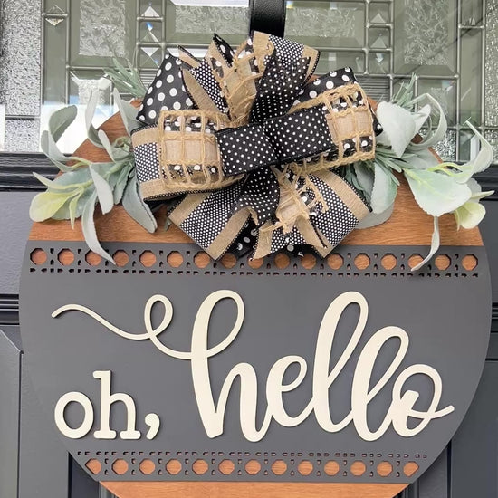 Modern farmhouse Oh Hello wood door hanger displayed on a black front door with designer bow and greenery.