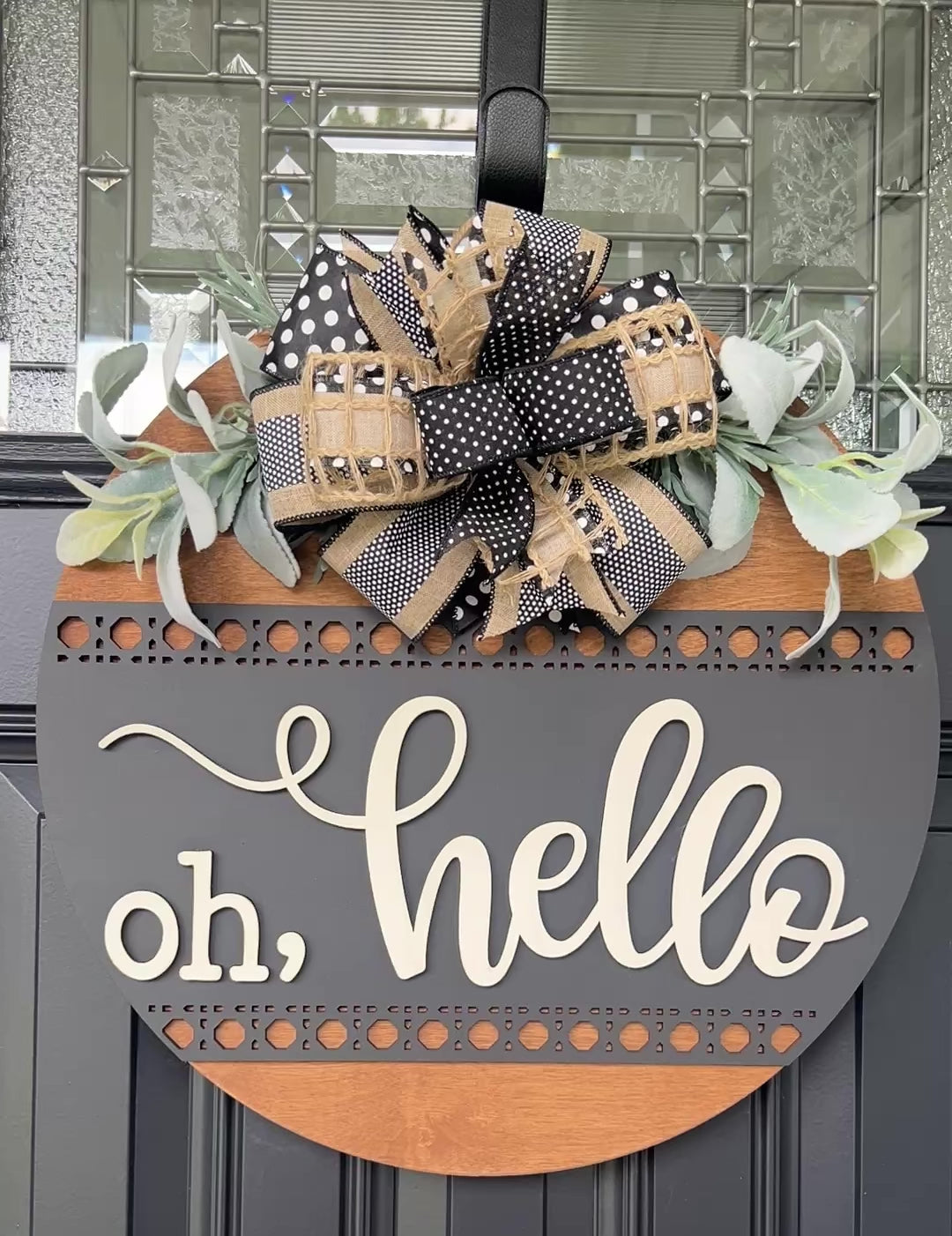 Modern farmhouse Oh Hello wood door hanger displayed on a black front door with designer bow and greenery.