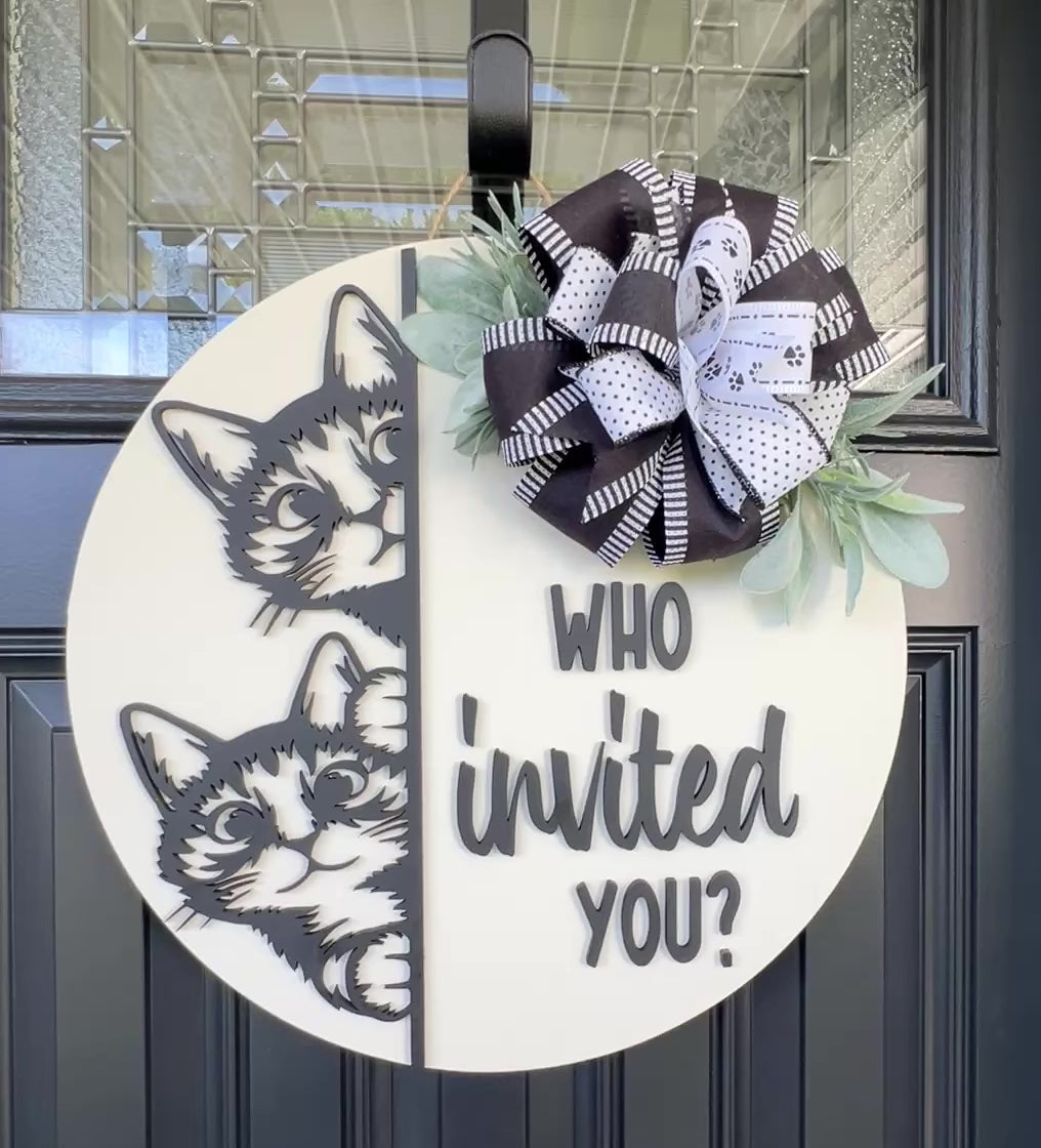 "Black and white cat-themed wooden door hanger with two cats and the phrase 'Who Invited You?' displayed on a front door."