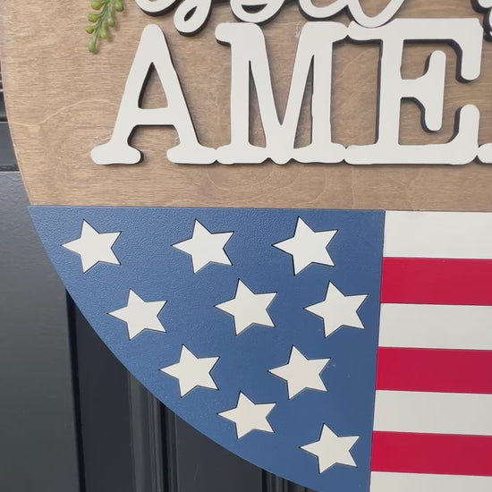 Decorative door hanger with 'God bless America' text and American flag design.