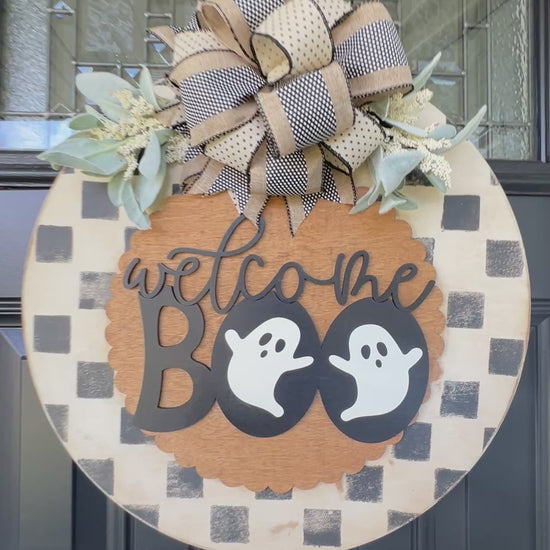 Handmade Welcome Boo Halloween door hanger with ghost accents, black and cream checkered background, layered wood lettering, designer bow, and fall front porch décor.