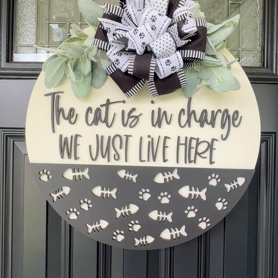The Cat is in Charge We Just Live Here door hanger on black front door with paw print bow and lambs ear greenery