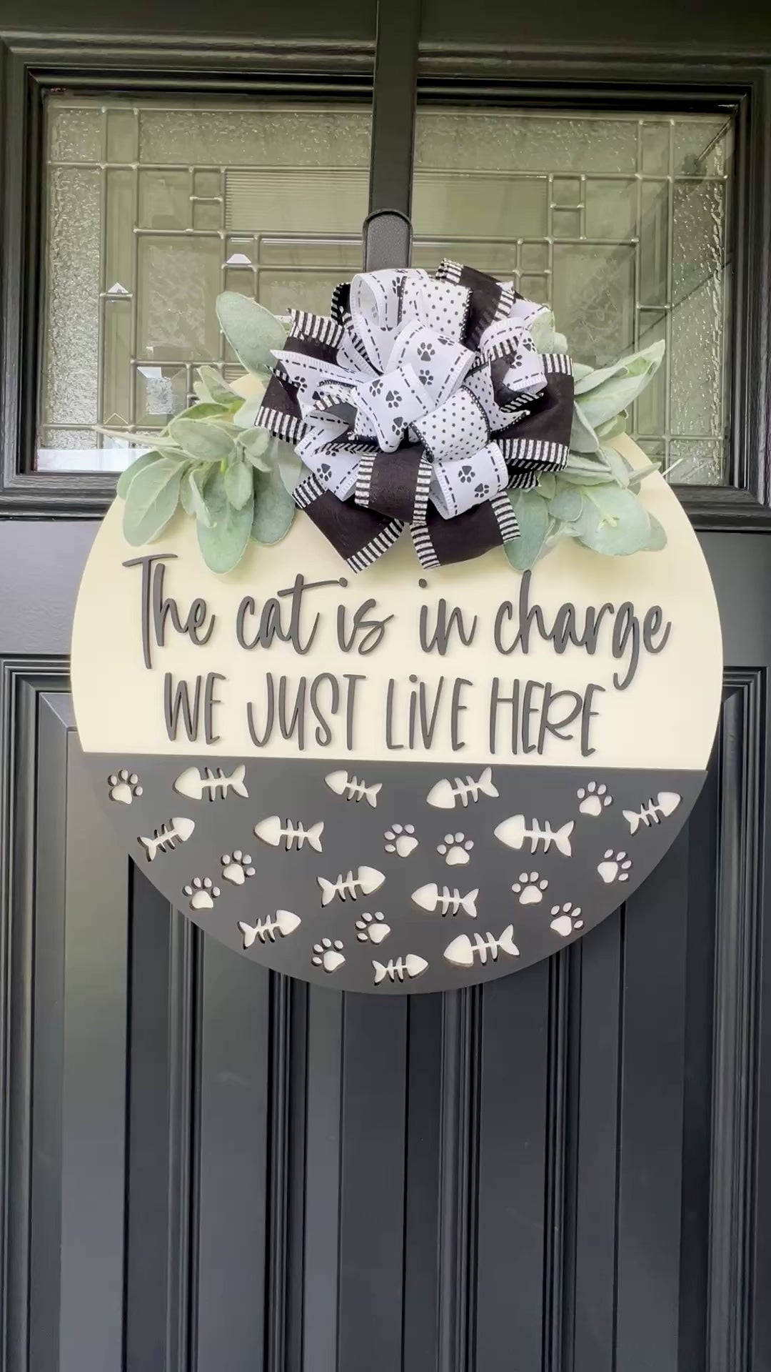 The Cat is in Charge We Just Live Here door hanger on black front door with paw print bow and lambs ear greenery