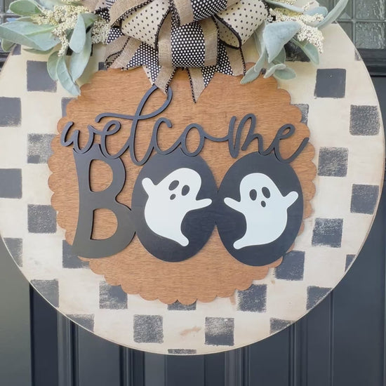 Handmade Welcome Boo Halloween door hanger with ghost accents, black and cream checkered background, layered wood lettering, designer bow, and fall front porch décor.