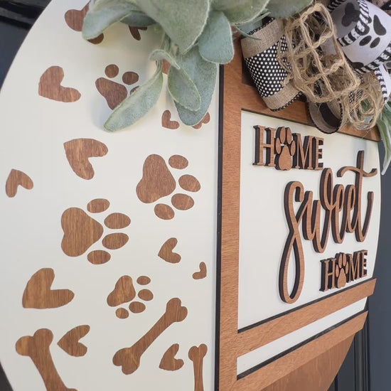 Handmade Home Sweet Home dog lover door hanger featuring laser-cut paw prints, dog bone accents, stained birchwood details, greenery, and a coordinating designer bow.