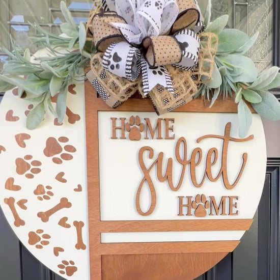 Handmade Home Sweet Home dog lover door hanger featuring laser-cut paw prints, dog bone accents, stained birchwood details, greenery, and a coordinating designer bow.