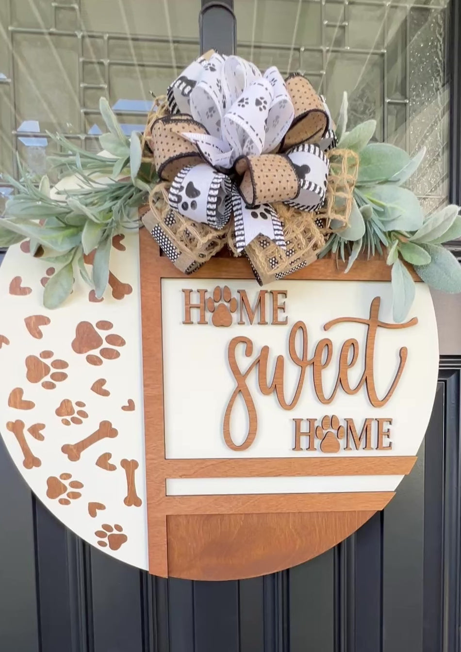 Handmade Home Sweet Home dog lover door hanger featuring laser-cut paw prints, dog bone accents, stained birchwood details, greenery, and a coordinating designer bow.