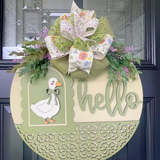 Handmade Hello goose wooden door hanger displayed on a black front door with farmhouse porch décor, showcasing sage green layered wood details, floral bow, and vintage goose design.