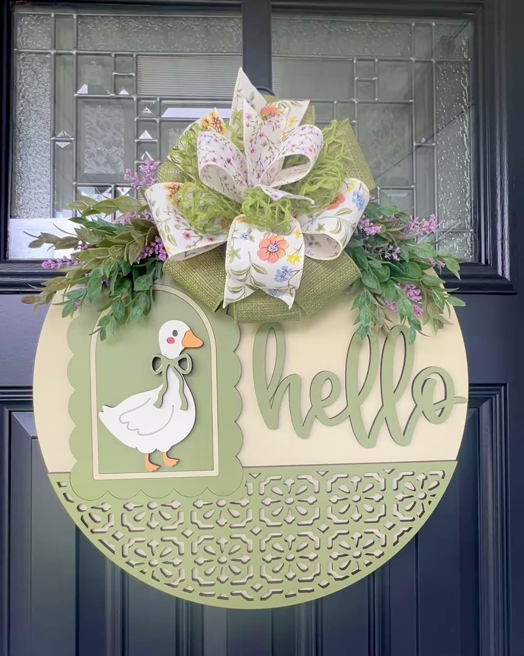 Handmade Hello goose wooden door hanger displayed on a black front door with farmhouse porch décor, showcasing sage green layered wood details, floral bow, and vintage goose design.