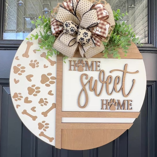 Handmade Home Sweet Home dog lover door hanger featuring laser-cut paw prints, dog bone accents, stained birchwood details, greenery, and a coordinating designer bow. 