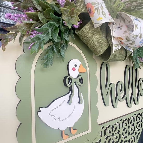 Side profile of a layered Hello goose wooden door hanger featuring a vintage goose, sage green accents, premium floral bow, and lush spring greenery for farmhouse front porch décor.