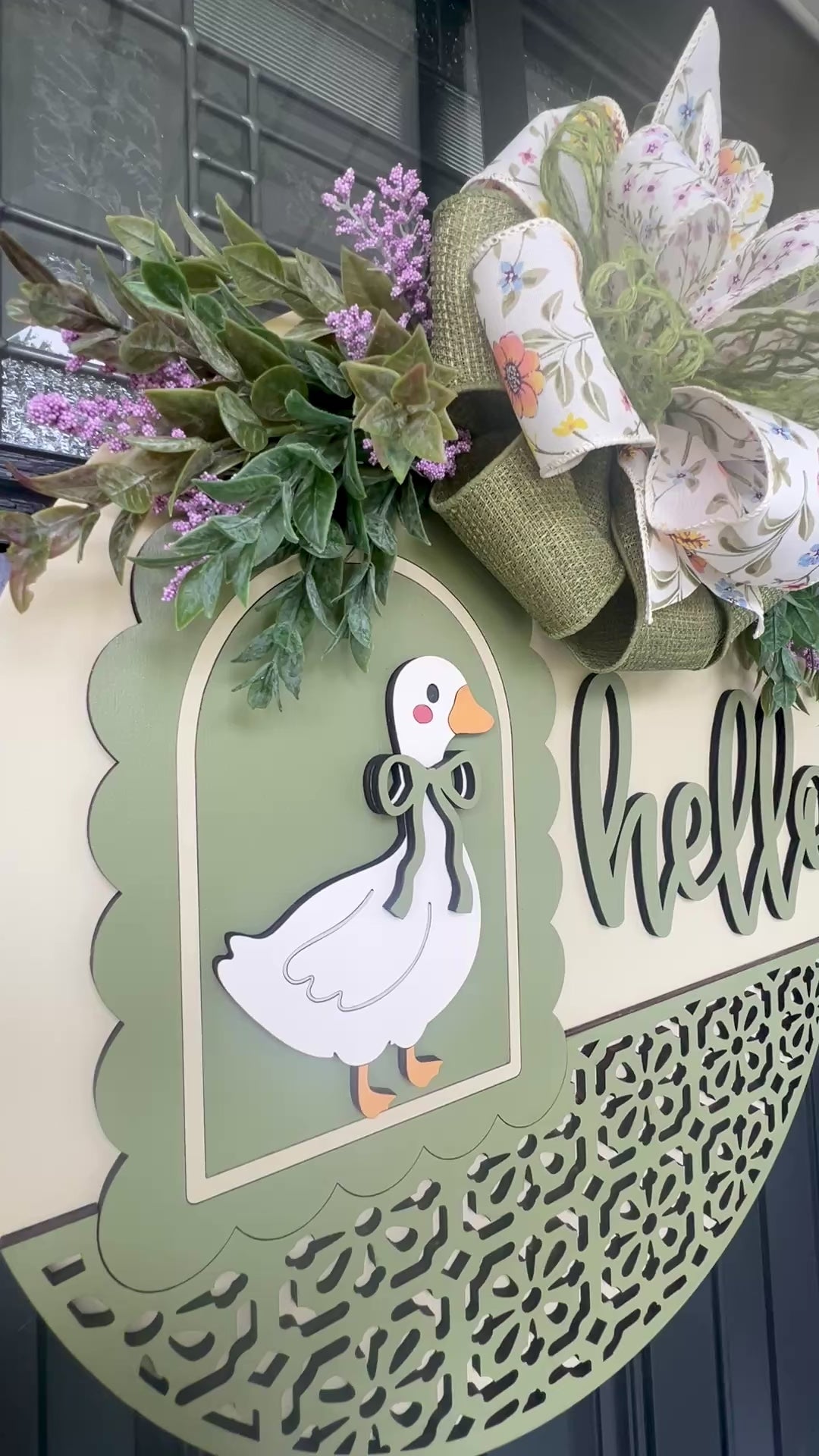Side profile of a layered Hello goose wooden door hanger featuring a vintage goose, sage green accents, premium floral bow, and lush spring greenery for farmhouse front porch décor.