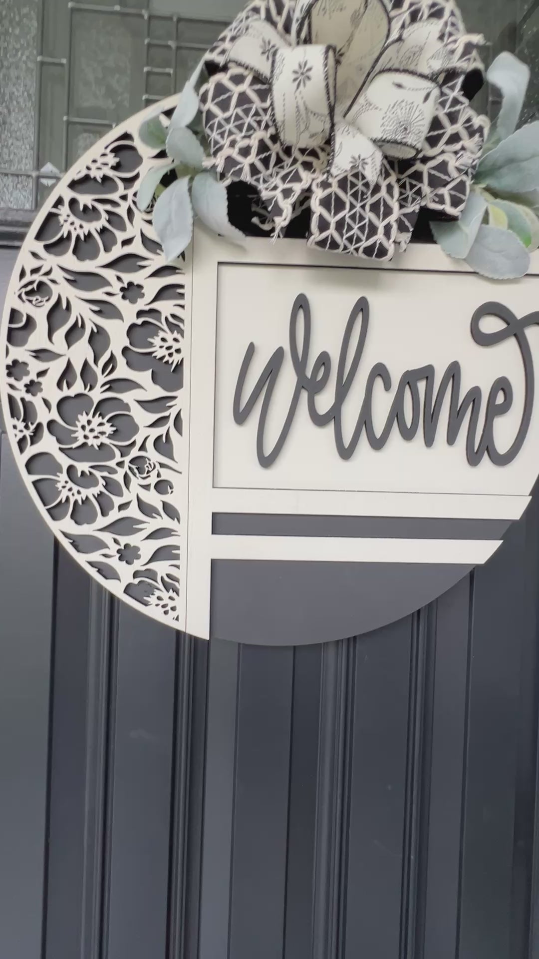 black and white welcome door hanger with floral cutout design
modern farmhouse front door sign with layered wood welcome script
18 inch round wooden welcome sign with decorative bow and greenery
neutral black white door hanger for front porch decor
handmade welcome sign with floral overlay and raised lettering
elegant entryway decor black and white round door hanger