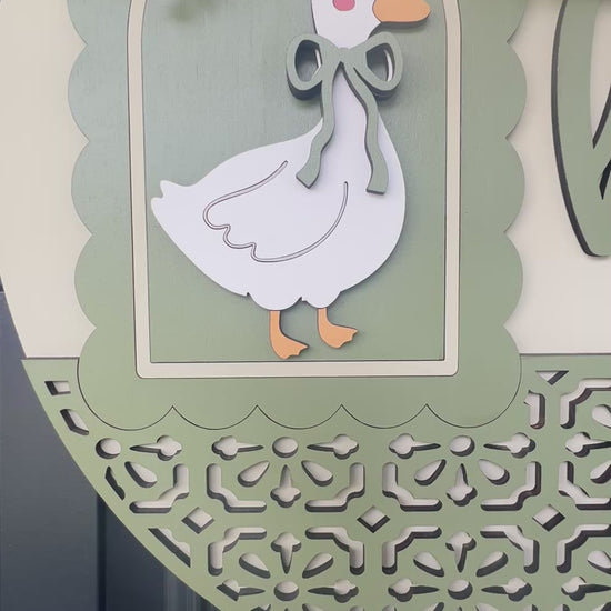 Handmade Hello goose wooden door hanger displayed on a black front door with farmhouse porch décor, showcasing sage green layered wood details, floral bow, and vintage goose design.