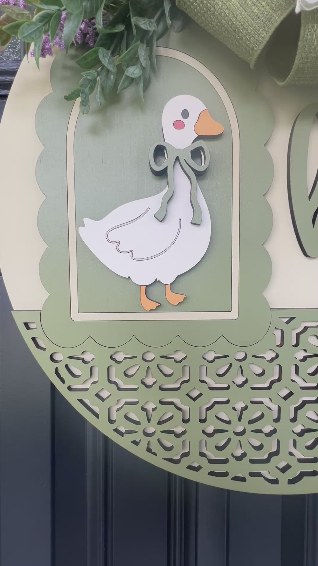 Handmade Hello goose wooden door hanger displayed on a black front door with farmhouse porch décor, showcasing sage green layered wood details, floral bow, and vintage goose design.