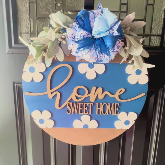 “Close-up of raised home sweet home lettering on blue floral door hanger”
“Blue and white bow with greenery on handmade home sweet home sign”