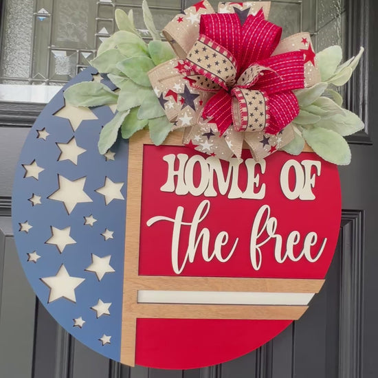 Decorative door hanger with 'Home of the Free' text and American flag design.