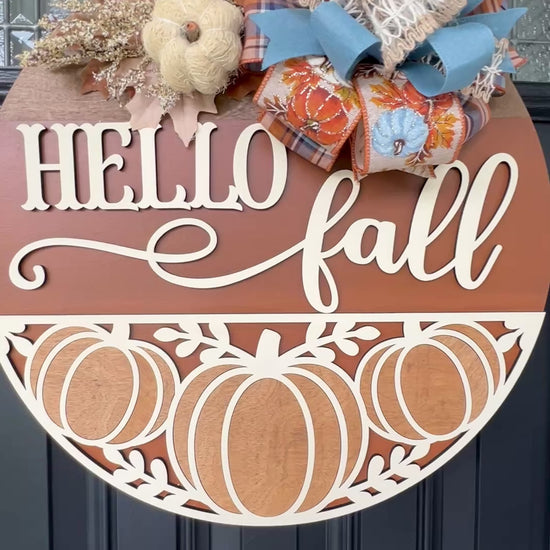 Hello Fall pumpkin door hanger with layered wood lettering, decorative pumpkin cutouts, designer bow, seasonal greenery, and autumn accents displayed on a front door.  Movie