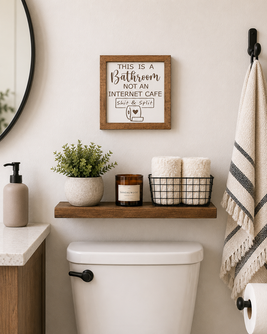 This Is a Bathroom Not an Internet Cafe engraved wood sign displayed above toilet in a modern farmhouse bathroom with floating shelf, candle, and woven basket